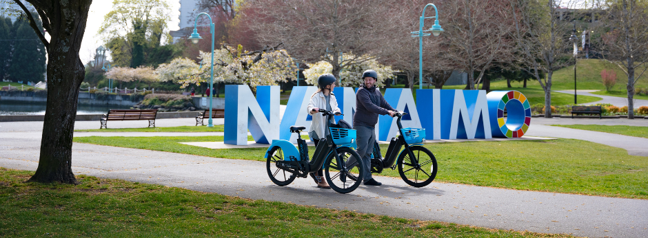 two cyclists in front of large Nanaimo sign